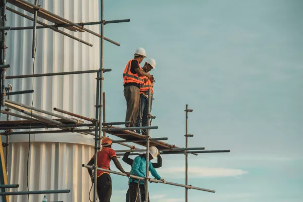 Construction workers in high visibility jackets on scaffolding working at a height discussing how to prevent workplace falls by using fall protection equipment.