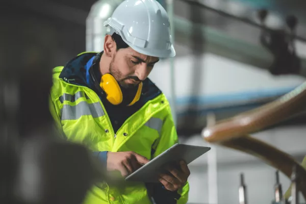 Construction worker looking at iPad considering the hierarchy of control when working from a height whilst wearing a hard hat and high visibility jacket.